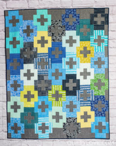 Blueberry Park Plus and Minus quilt hanging on brick wall