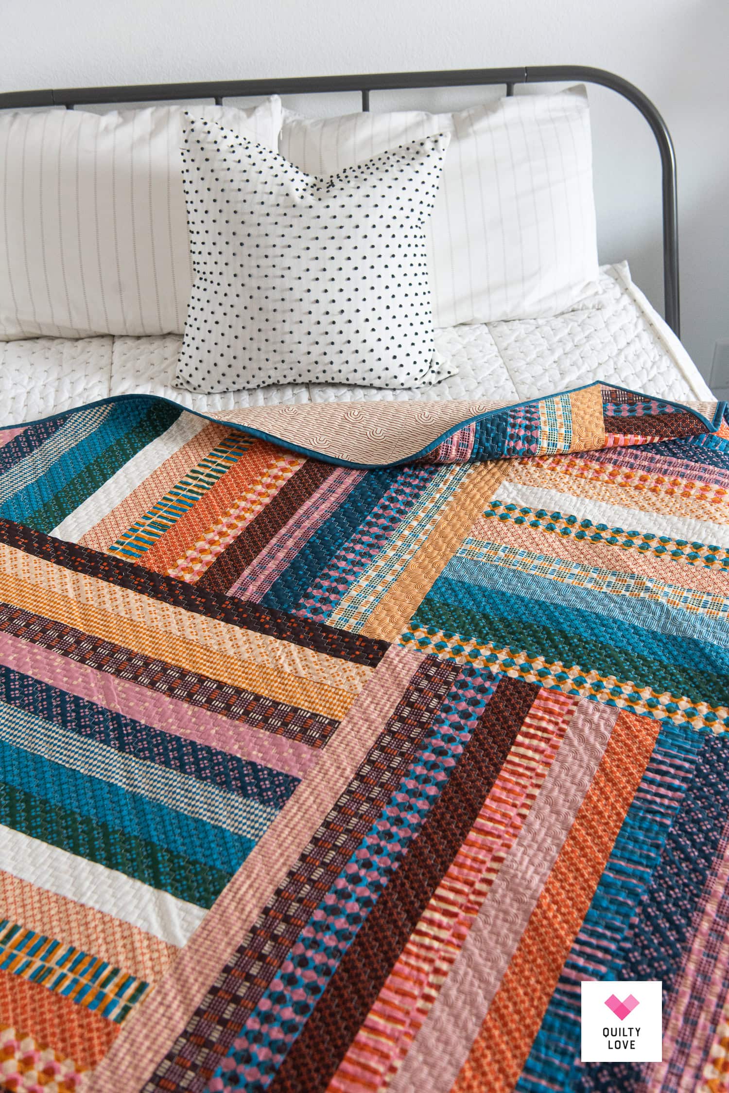Vibrant patchwork quilt on a bed with white pillows and a polka dot cushion.