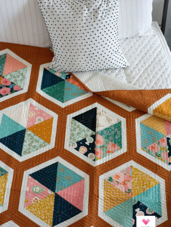 A Triangle Hexies quilt arranged on a bed with a polka dot pillow