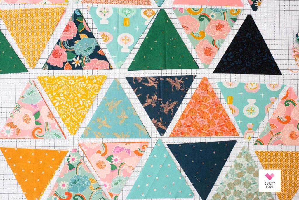 Quilting fabrics cut into triangles on a white cutting mat