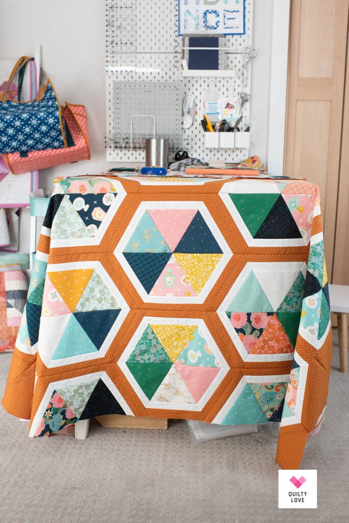 A Triangle Hexies quilt top draped over a table in a sewing room