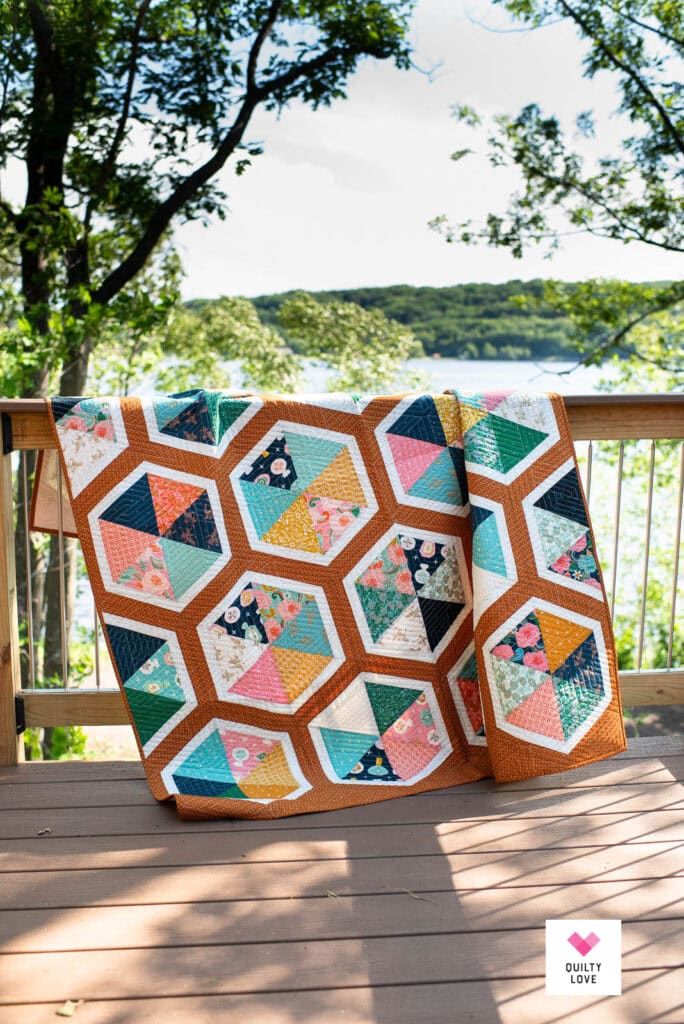 A Triangle Hexies quilt on a railing with water in the background