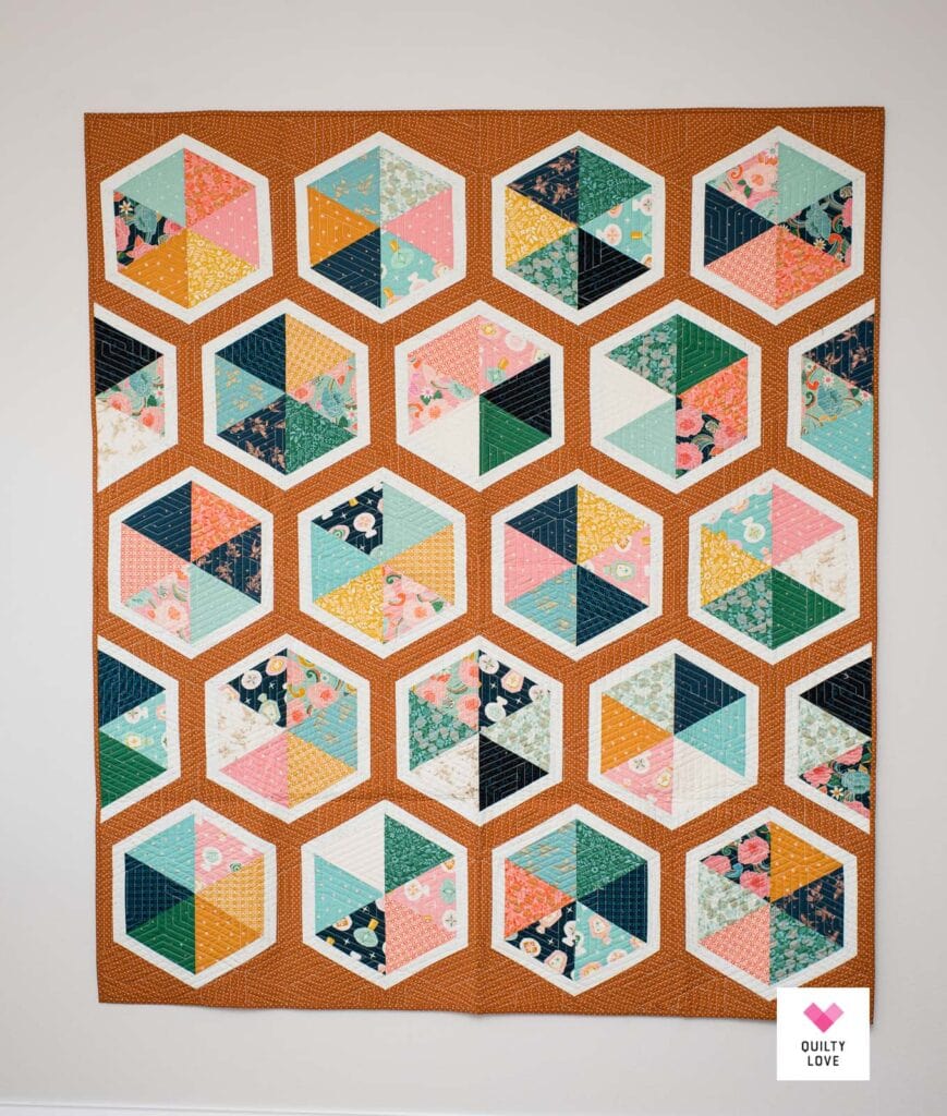 A quilt on a wall made up of hexies with white sashing and a polka dot background